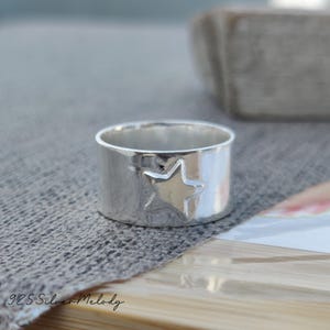 May include: A silver ring with a star cut-out design. The ring is wide and has a polished finish.