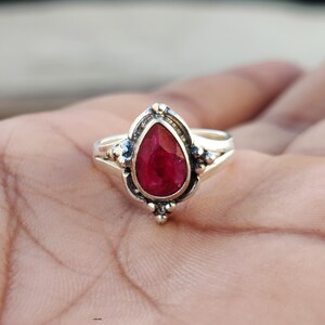 May include: A silver ring with a pear-shaped ruby gemstone set in a detailed silver setting.