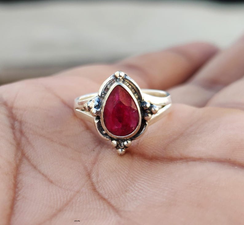 May include: A silver ring with a pear-shaped ruby gemstone set in a detailed silver setting.