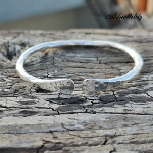 May include: A silver hammered bangle bracelet with a slightly open design. The bracelet is made of 925 sterling silver and has a textured finish.