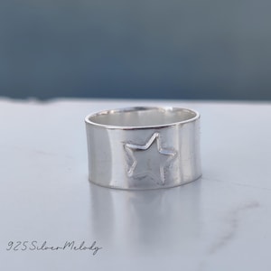 May include: A silver ring with a star design. The ring is wide and has a smooth, polished finish.