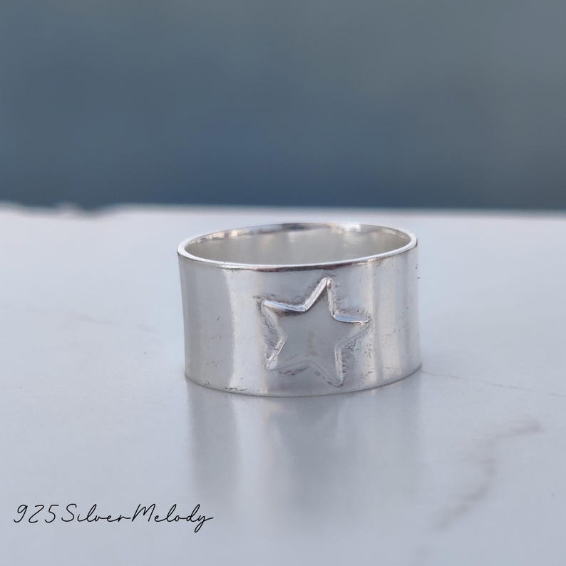 May include: A silver ring with a star design. The ring is wide and has a smooth, polished finish.