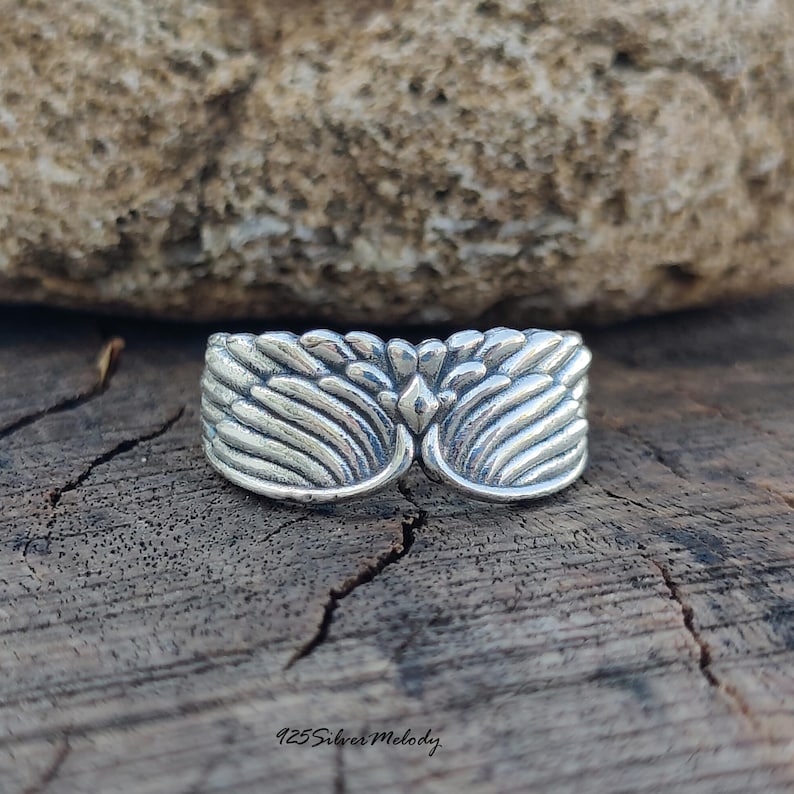 May include: A sterling silver ring featuring a detailed wing design that wraps around the band. The metal has a polished finish with darkened recessed areas to highlight the feather textures. The text 925 Silver Melody is printed below.