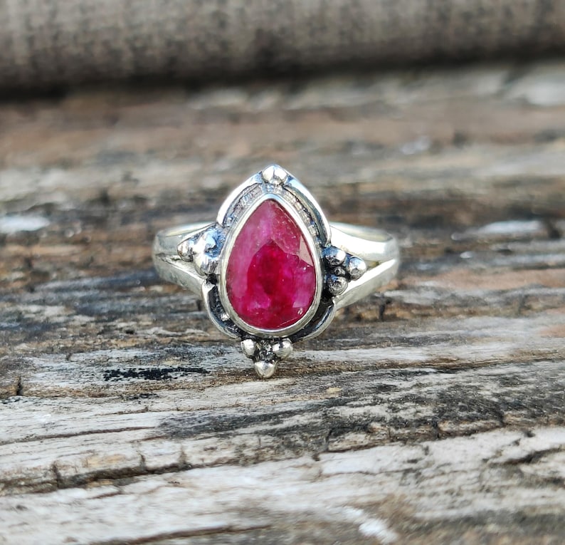 May include: A silver ring with a pear-shaped ruby gemstone set in a detailed silver setting.