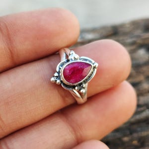 May include: A silver ring with a teardrop-shaped ruby gemstone set in a delicate filigree design.