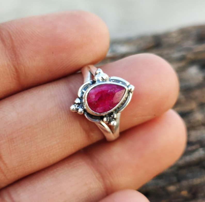 May include: A silver ring with a teardrop-shaped ruby gemstone set in a delicate filigree design.