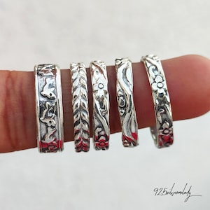 May include: Five silver rings with detailed designs. The rings feature patterns of leaves, flowers, and other nature-inspired motifs. The rings are displayed on a finger, showcasing their intricate craftsmanship and design.