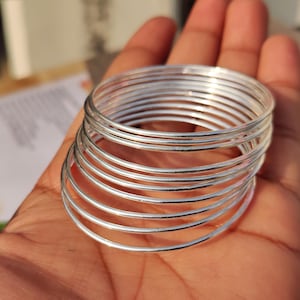 Può includere: Un set di braccialetti d'argento, un gioiello tradizionale indiano, disposti in un motivo circolare.