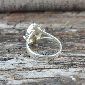 May include: Silver ring with a large, faceted gemstone. The ring is shown from the side, with the band visible.