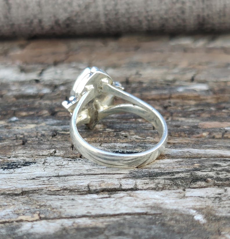 May include: Silver ring with a large, faceted gemstone. The ring is shown from the side, with the band visible.