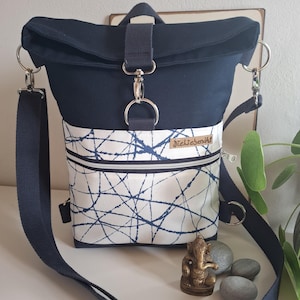 Könnte beinhalten: Marineblaue und weiße Umhängetasche mit Klappenverschluss. Die Tasche hat ein weißes Panel mit blauem Spritzmuster und eine Reißverschlusstasche. Die Tasche hat einen verstellbaren marineblauen Riemen und silberfarbene Hardware. Das Etikett lautet "dieLiebenäht".