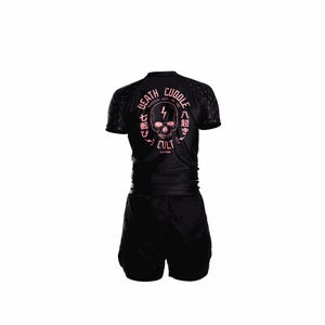 Könnte beinhalten: Schwarzes Sport-Top und -Shorts-Set. Das Top zeigt eine rosa Totenkopf-Grafik mit den Worten "Death Cuddle" und japanischen Schriftzeichen. Das Set ist für sportliche Aktivitäten konzipiert.