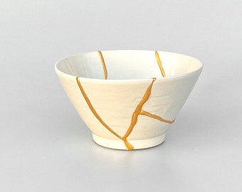 May include: White ceramic bowl with gold crackle design. The bowl is a traditional Japanese style.