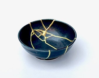 May include: A small, dark blue ceramic bowl with a crackled glaze. The cracks are filled with a gold-coloured glaze, creating a decorative pattern.