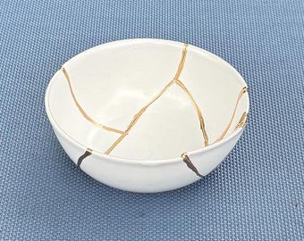 Peut inclure: Un bol en céramique blanche avec des lignes de craquelure dorées. Le bol est de style japonais traditionnel.