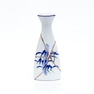 May include: White ceramic sake bottle with blue bamboo design and gold-coloured kintsugi repair lines. The bottle has a narrow neck and a dark blue rim. A traditional Japanese aesthetic.
