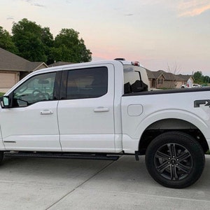 Op de afbeelding: Een witte Ford F-150 pick-up truck met zwarte wielen en de tekst "FX4 OFF-ROAD" op de achterklep.