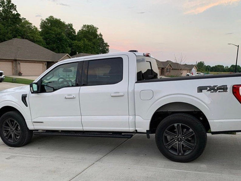 Op de afbeelding: Een witte Ford F-150 pick-up truck met zwarte wielen en de tekst "FX4 OFF-ROAD" op de achterklep.