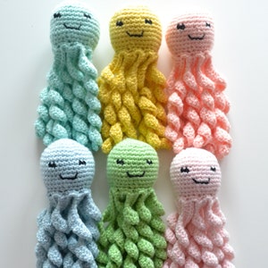 Op de afbeelding: Zes handgemaakte gehaakte octopus speelgoed in pastelkleuren: lichtblauw, geel, roze, blauw, groen en lichtroze. Elke octopus heeft een lachend gezicht met zwart geborduurde ogen en mond. De tentakels zijn strak gehaakt.
