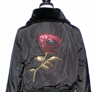 Puede incluir: Chaqueta bomber negra con cuello de piel sint&eacute;tica y un gran dise&ntilde;o de rosa de lentejuelas en la espalda.