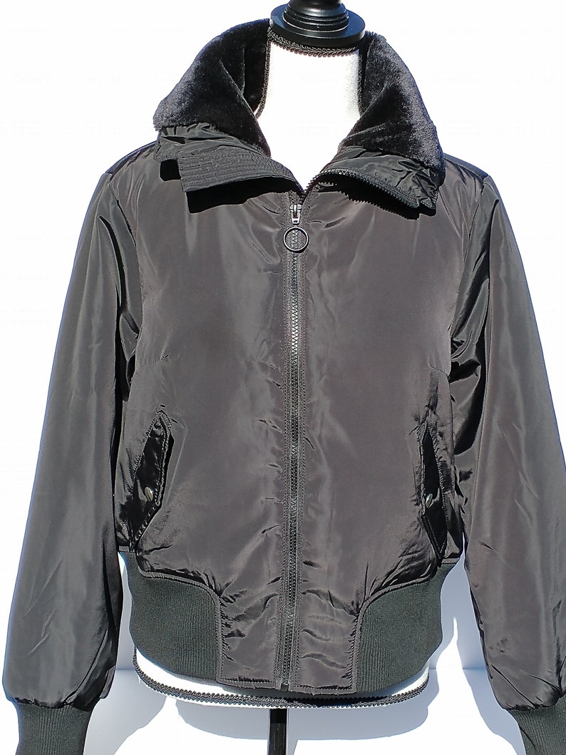 Puede incluir: Una chaqueta bomber negra con cuello de piel sint&eacute;tica y cierre de cremallera. La chaqueta tiene cintura y pu&ntilde;os de canal&eacute;.