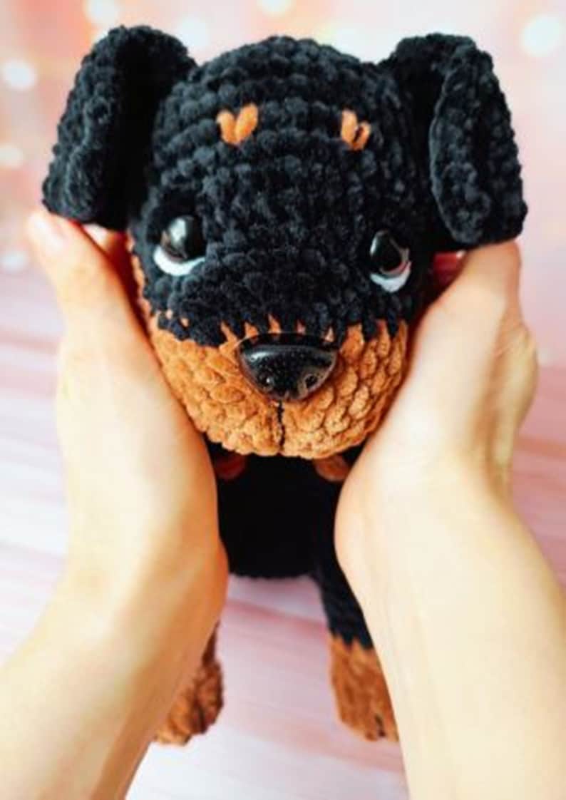 May include: A crocheted plush toy dog with black and brown fur. The dog is being held in the hands of a person.