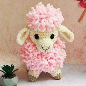 May include: A pink and white crocheted stuffed sheep toy. The sheep has a fluffy pink body and a white face with black eyes.