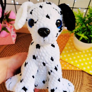 Puede incluir: Peluche de perro dálmata hecho a mano con manchas blancas y negras. El peluche tiene ojos azules y detalles negros en las orejas y la nariz. El perro está sentado y el peluche está hecho de un material suave y texturizado.