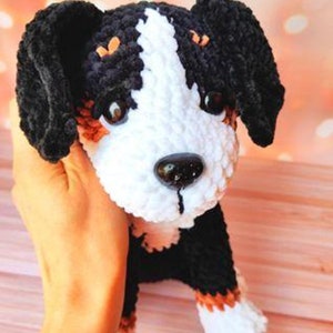 May include: A crocheted stuffed dog toy with black, white, and brown fur. The dog has a white face with black eyes and a black nose.