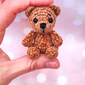 May include: A small, handmade brown teddy bear with black eyes and a black nose. The bear is made of a textured, plush material and has a classic teddy bear shape. The bear is approximately 3 inches tall, perfect for a child's toy or a collector's item.