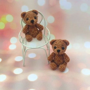 May include: Two handmade brown crochet teddy bears. One teddy bear is sitting on a small white chair, and the other is sitting on the surface. The bears have black eyes and noses. The background is a soft pink with bokeh lights.