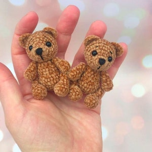 May include: Two small, handmade brown teddy bears with black eyes and noses. The bears are made of a soft, textured material and have a classic teddy bear shape. They are shown in a person's hand.