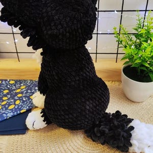 Puede incluir: Un juguete de peluche hecho a mano, un perro negro y blanco, elaborado con hilo suave y texturizado. El perro est&aacute; sentado, con la cola extendida. Tiene patas blancas y una cola esponjosa.
