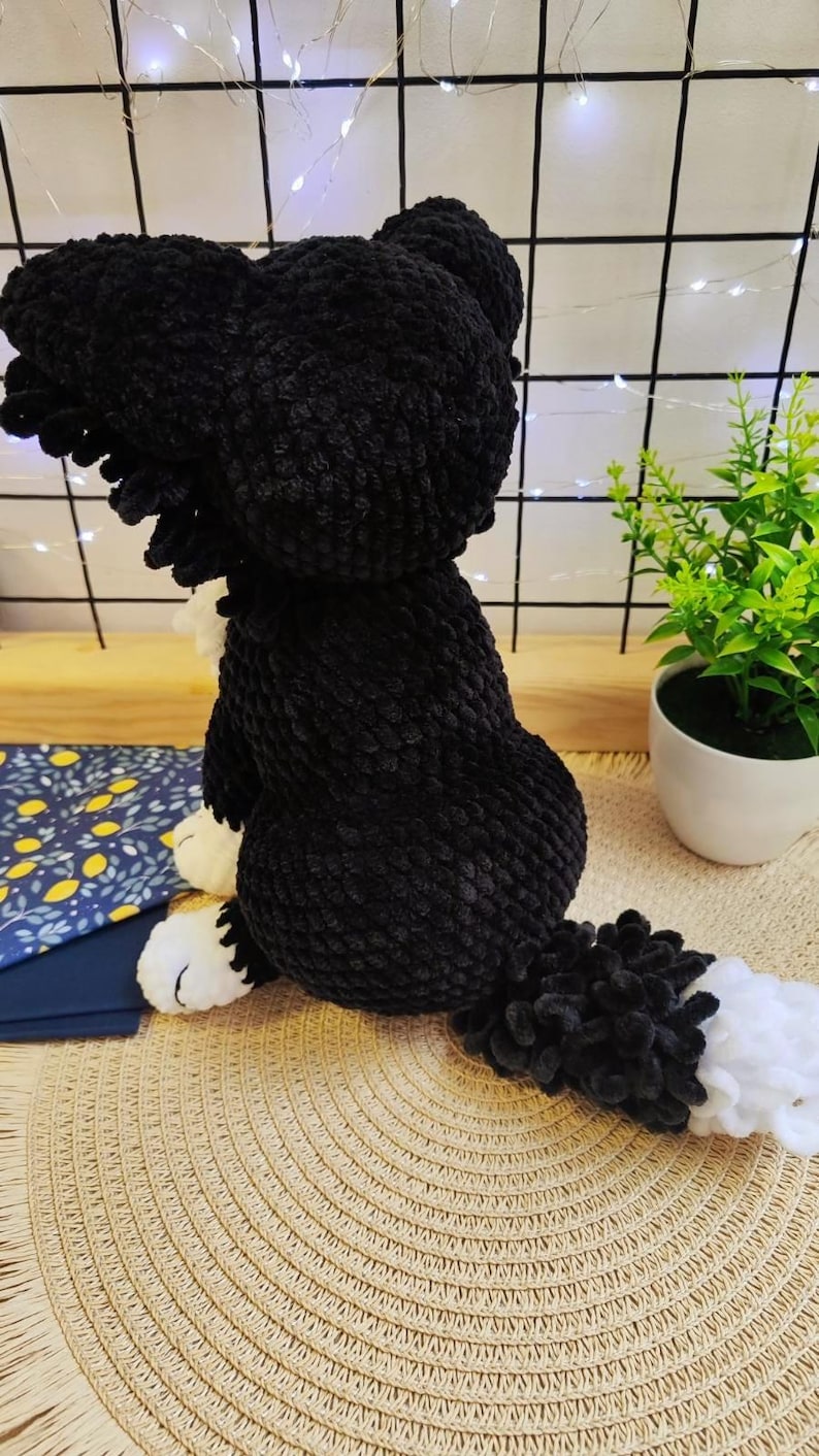 Puede incluir: Un juguete de peluche hecho a mano, un perro negro y blanco, elaborado con hilo suave y texturizado. El perro est&aacute; sentado, con la cola extendida. Tiene patas blancas y una cola esponjosa.