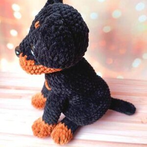 May include: A black and orange crocheted plush toy dog. The dog is sitting on a wooden surface.