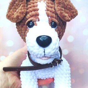 Op de afbeelding: Een gehaakte pluche speelgoedhond met bruin en wit bont, met een bruin leren halsband. De hond heeft zwarte ogen en een zwarte neus.