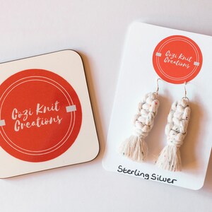 May include: A coaster and a pair of earrings. The coaster and earring card both feature a red circle with the text "Cozi Knit Creations". The earrings are white macrame with colourful flecks and sterling silver hooks. The earring card reads "Sterling Silver".