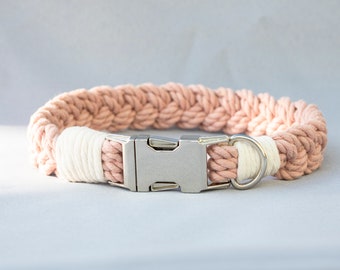 May include: A braided dog collar in shades of pink and white, featuring a silver metal buckle and a D-ring. The collar is made of thick, woven rope, creating a sturdy and stylish accessory for pets.