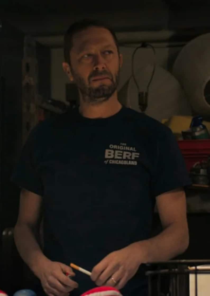 Peut inclure: Un homme portant un t-shirt bleu fonc&eacute; avec le texte "The Original Berf of Chicagoland" imprim&eacute; sur le devant. Il tient une cigarette dans sa main droite.