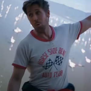 May include: A light grey t-shirt with red trim around the collar and sleeves. The shirt displays the text "HORSE SHOE BEND AUTO CLUB" with checkered flags. The person is wearing red trousers.