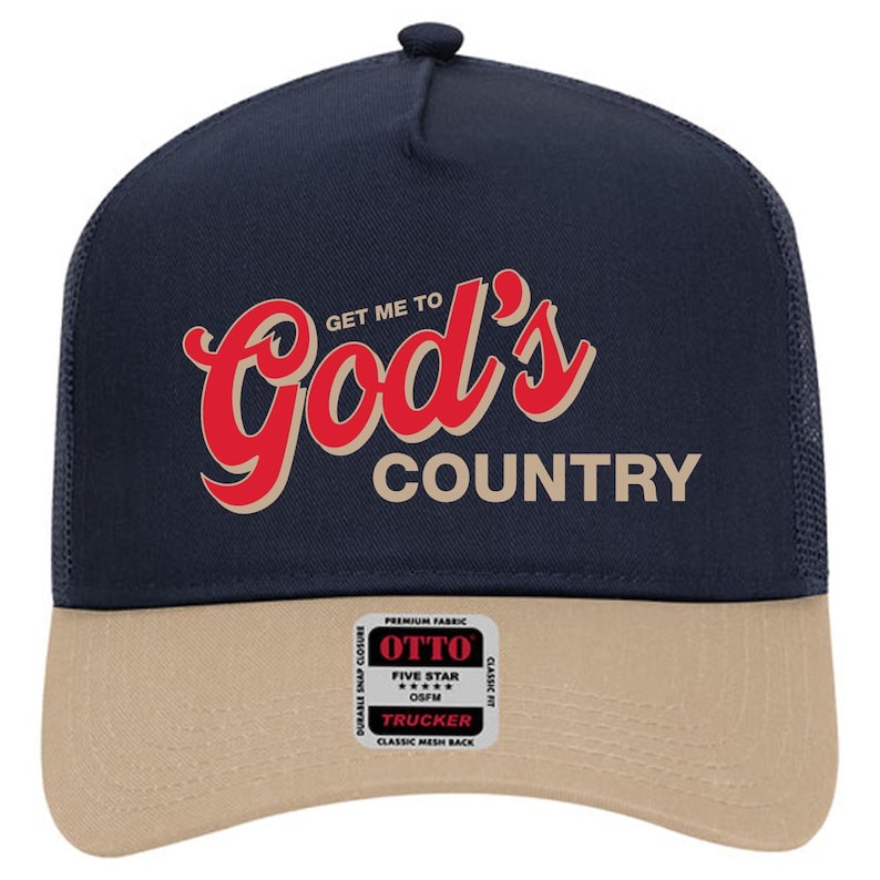 May include: Navy blue and tan trucker hat with the text "GET ME TO God's COUNTRY" in red and beige lettering. The hat features a mesh back and a snap closure. A small tag with the brand name is visible.