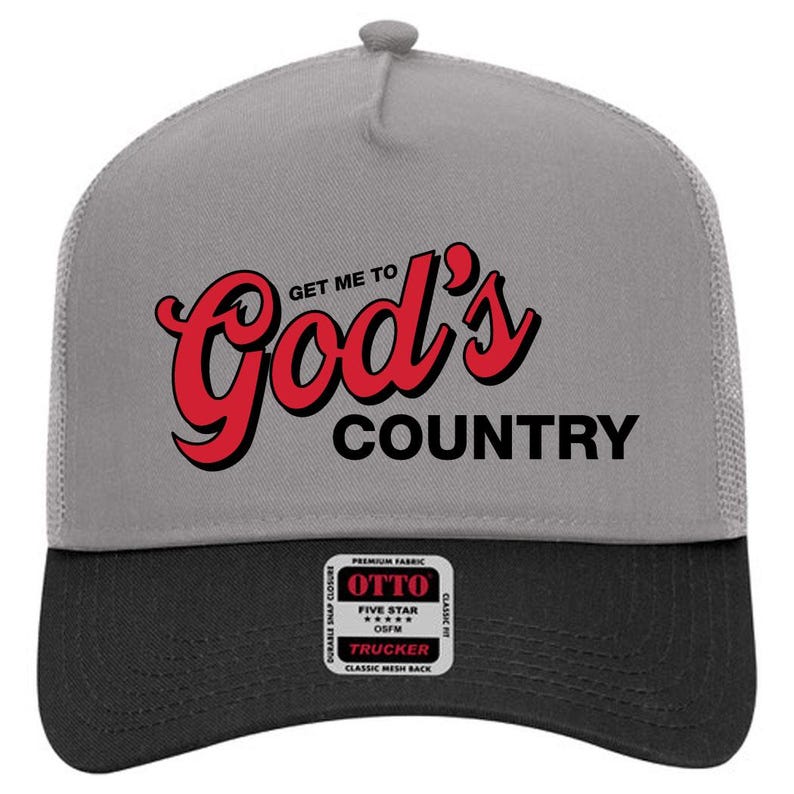 May include: A gray and black trucker hat with the text "Get Me To God's Country" in red and black. The hat has a mesh back and a snap closure. The hat also has a small patch that says "OTTO".