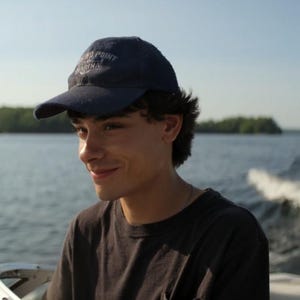 May include: A navy blue baseball cap with a curved brim and white embroidered text that reads "SAND POINT MARINA" on the front panel. The cap features a structured crown and a fabric strap closure at the back, designed for a casual, everyday look.