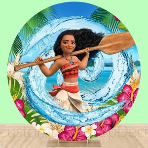 May include: A round, colorful backdrop featuring a cartoon image of Moana from the Disney movie Moana. Moana is holding a wooden paddle and is standing in front of a blue wave. The backdrop is surrounded by tropical flowers and leaves.