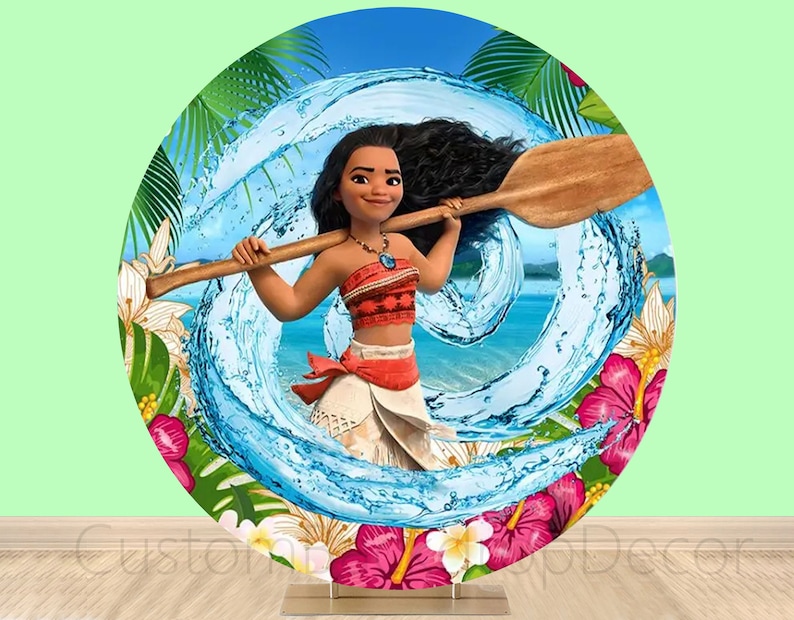 May include: A round, colorful backdrop featuring a cartoon image of Moana from the Disney movie Moana. Moana is holding a wooden paddle and is standing in front of a blue wave. The backdrop is surrounded by tropical flowers and leaves.