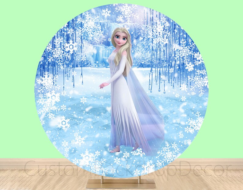 Puede incluir: Un tel&oacute;n de fondo redondo con una escena de invierno con un esquema de color blanco, azul y plateado. Un personaje femenino con cabello largo y rubio y un vestido blanco se encuentra en el centro del tel&oacute;n de fondo. El tel&oacute;n de fondo es perfecto para una fiesta con tem&aacute;tica de Frozen.