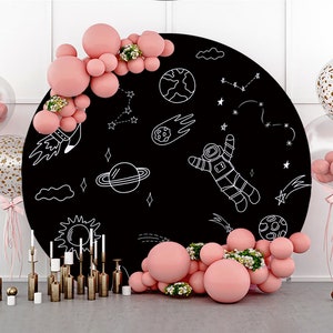 Op de afbeelding: Een zwarte ronde achtergrond met witte krijttekeningen van een astronaut, planeten, sterren en een komeet. Rondom de achtergrond zijn roze ballonnen gerangschikt.
