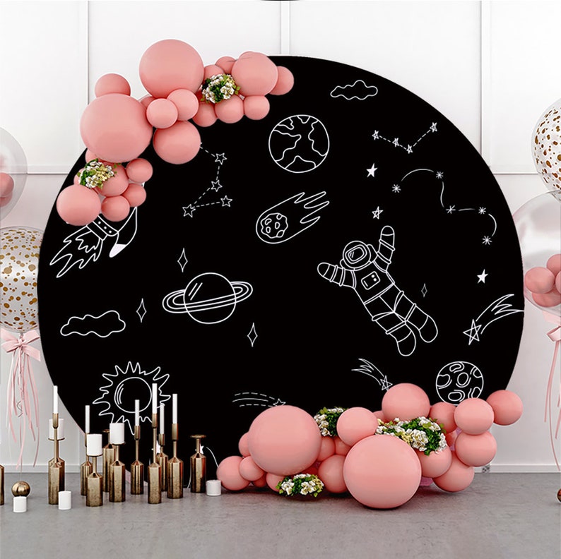 Op de afbeelding: Een zwarte ronde achtergrond met witte krijttekeningen van een astronaut, planeten, sterren en een komeet. Rondom de achtergrond zijn roze ballonnen gerangschikt.