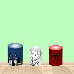 May include: Three round cardboard cake stands with different designs. The first stand is blue with a cityscape design. The second stand is white with a black spiderweb design. The third stand is red with a black spider design.