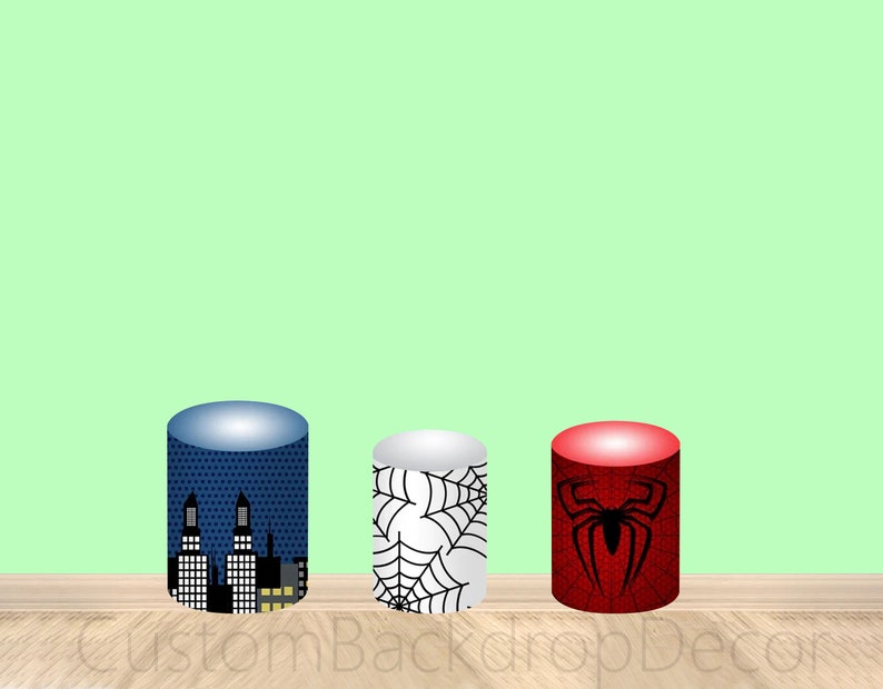 May include: Three round cardboard cake stands with different designs. The first stand is blue with a cityscape design. The second stand is white with a black spiderweb design. The third stand is red with a black spider design.